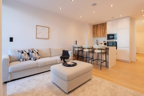 A modern living room with a sofa, ottoman, and a small bar area with stools.