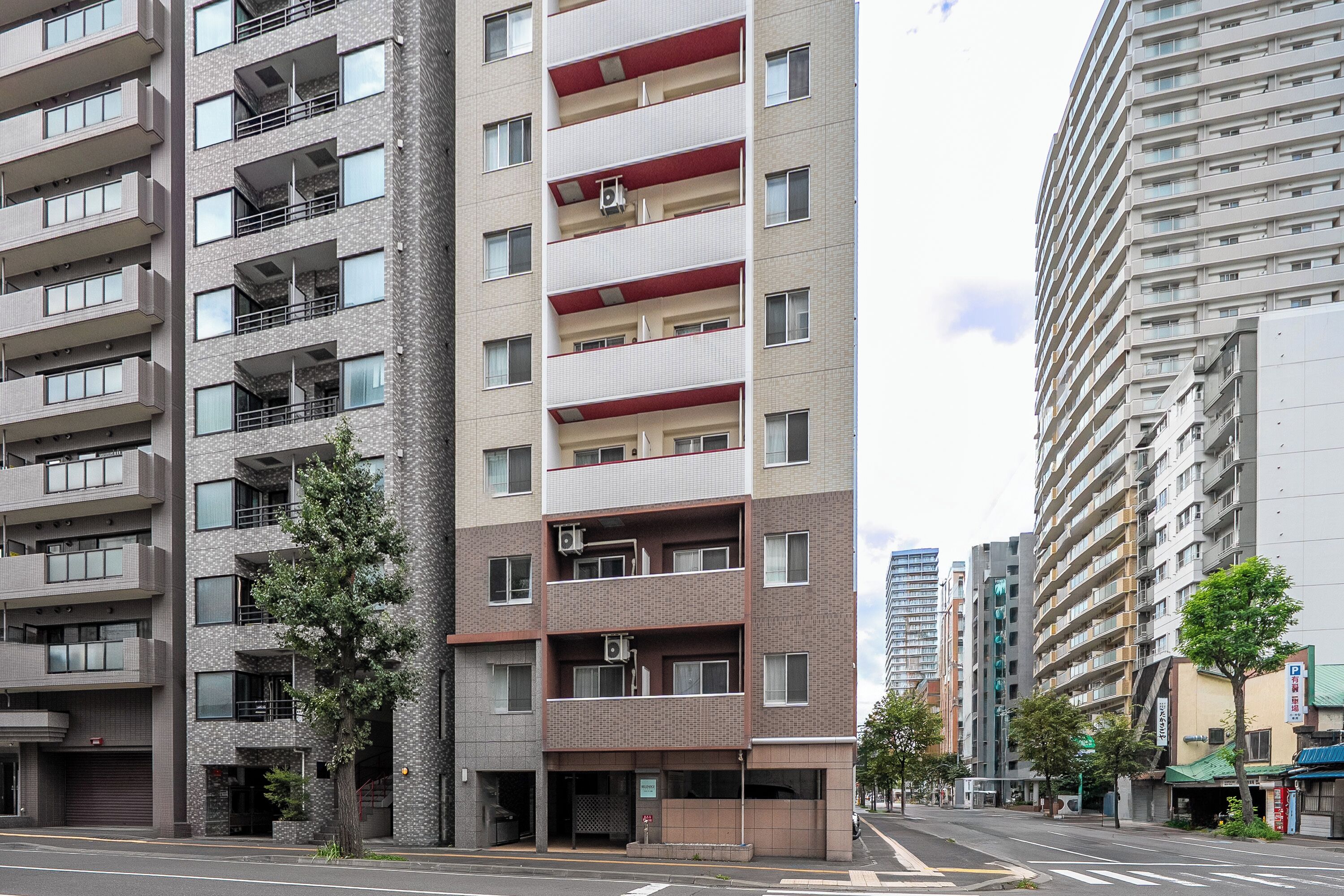 A multi-story residential building with balconies, air conditioning units, and a street view with a crosswalk.