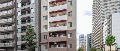 A multi-story residential building with balconies, air conditioning units, and a street view with a crosswalk.