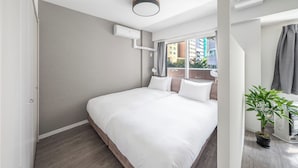 A modern hotel room with a large bed, a potted plant, and a view of the city through the window. - BELLE NEIGE 305 (Sapporo)