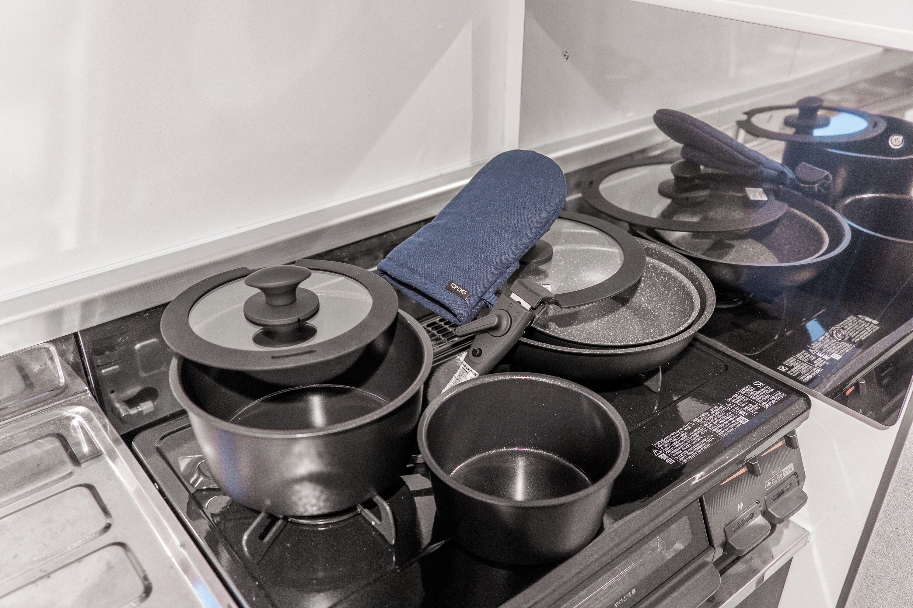 A kitchen with four black pots on a stove, a blue oven mitt, and a white wall in the background.