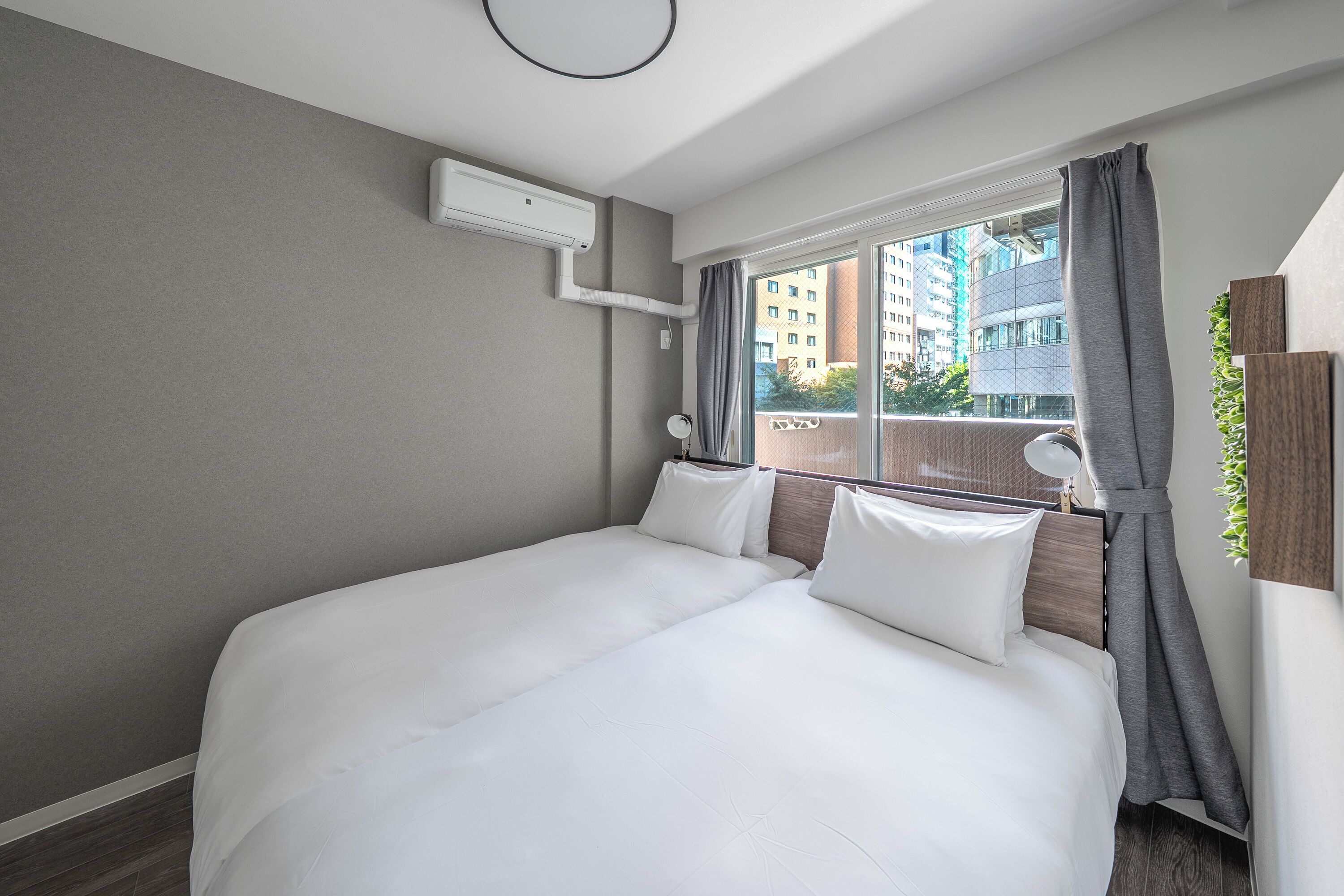 Une chambre d’hôtel moderne dotée d’un grand lit, d’une fenêtre avec des rideaux, d’un climatiseur fixé au mur et offrant une vue sur les bâtiments environnants.