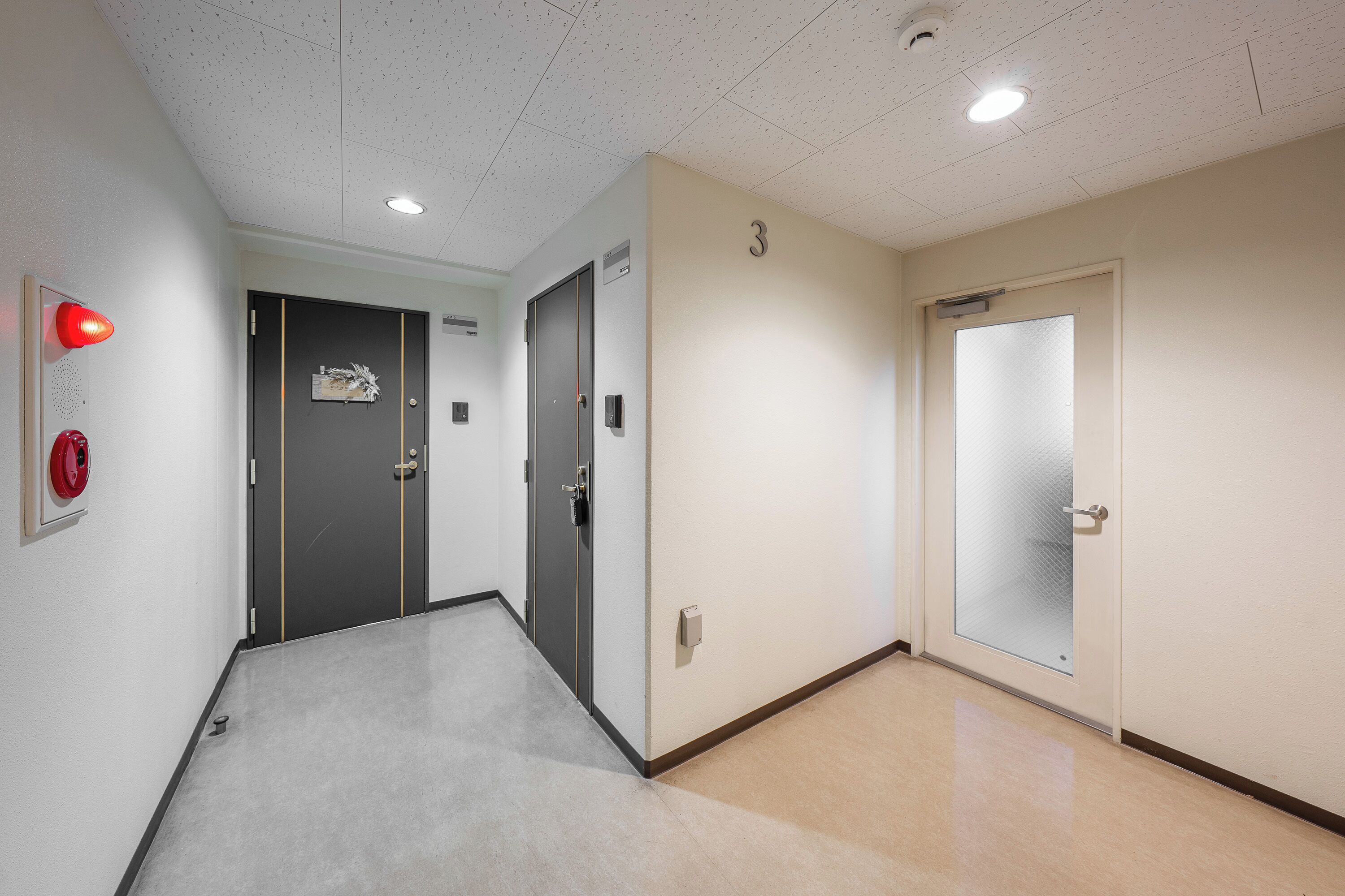 A hallway with a grey carpet, a fire alarm, and two doors, one with a number 3 sign.