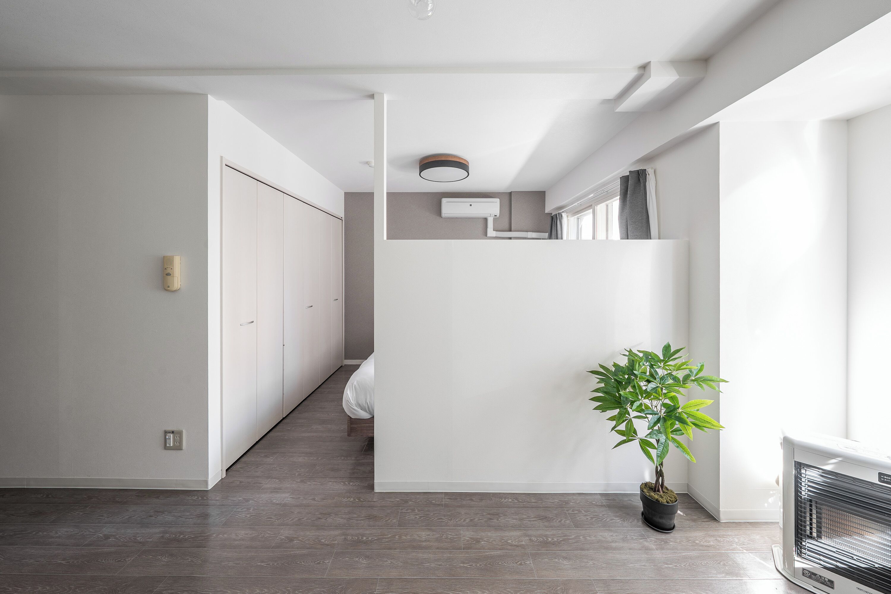A modern hallway with a potted plant, a ceiling-mounted air conditioning unit, and a radiator.