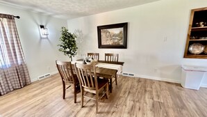 A dining area with a wooden table and chairs, a potted plant, and a framed picture on the wall. - Homestead House - Simple comfort in the heart of Kansas (Hoisington)