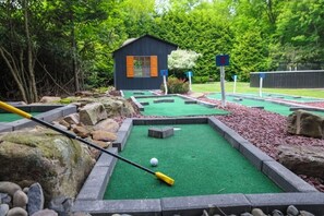 Un campo de mini golf con un pequeño edificio, césped artificial verde y varios obstáculos.