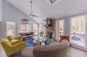 Un salón amplio con chimenea, ventanas grandes y ventilador de techo.