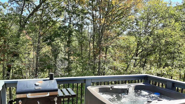A hot tub on a wooden deck with a barbecue grill.