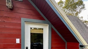 A red building with a white door, a small porch with a bench, and a welcome mat.