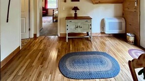 A room with wooden flooring, a ceiling fan, a white door, a blue rug, a wooden cabinet, and a microwave.