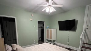 Une chambre à coucher avec un lit, un ventilateur de plafond, une télévision et un escalier.