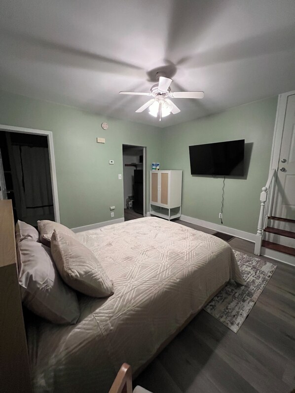 Une chambre à coucher avec un lit, un ventilateur de plafond, une télévision et un escalier.