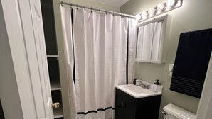 Une salle de bain avec des toilettes blanches, un lavabo, un miroir et un rideau de douche.