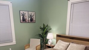Une chambre à coucher avec un lit, une chaise, une table de chevet avec une lampe et une plante en pot.