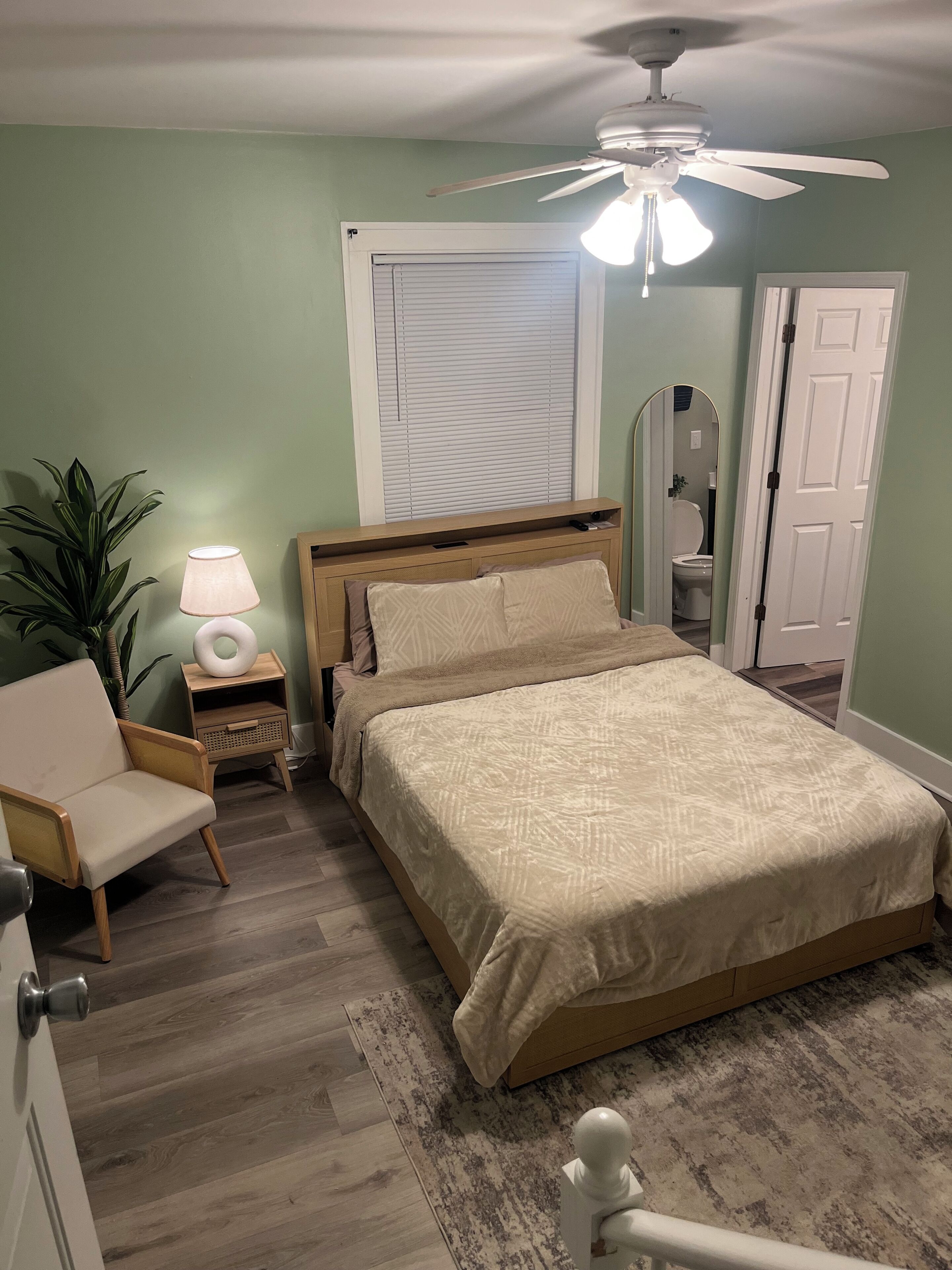 A bedroom with a bed, bedside table, lamp, chair, and a ceiling fan.