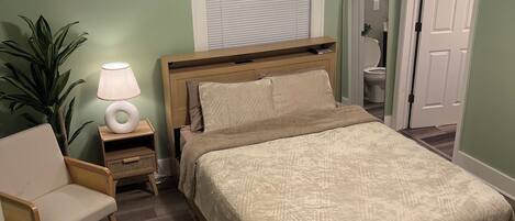 A bedroom with a bed, bedside table, lamp, chair, and a ceiling fan.