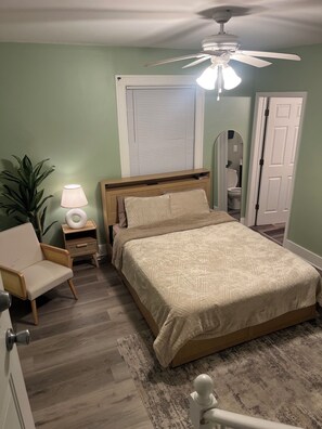 Une chambre à coucher comprenant un lit, une table de chevet, une lampe, une chaise et un ventilateur de plafond.