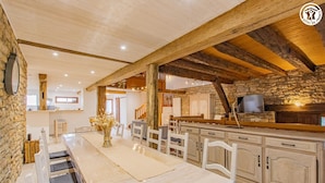 A spacious kitchen with a long dining table, wooden beams, and a stone wall. - Le Thiellet - SAINT USUGE (SAINT USUGE)