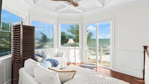 A spacious room with a large window overlooking the beach, a ceiling fan, and a white upholstered sofa. - 7791 Highway A1A (Melbourne Beach)