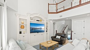 A spacious living room with a large flat-screen TV, white cabinetry, a leather sofa, and a wooden coffee table. - 7791 Highway A1A (Melbourne Beach)