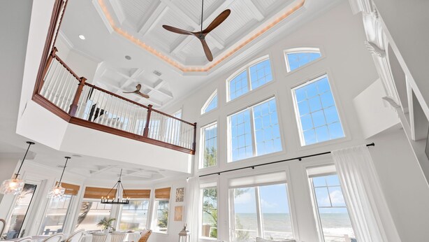 A spacious interior with a high ceiling, large windows, and a balcony overlooking the ocean. - 7791 Highway A1A (Melbourne Beach)