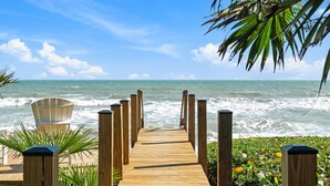 A wooden pier leading to the ocean with a chair and plants nearby. - 7791 Highway A1A (Melbourne Beach)