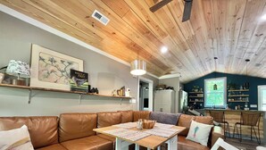 Un salon chaleureux avec un canapé d’angle en cuir marron, une table basse en bois et un coin repas comprenant une table et des chaises blanches.