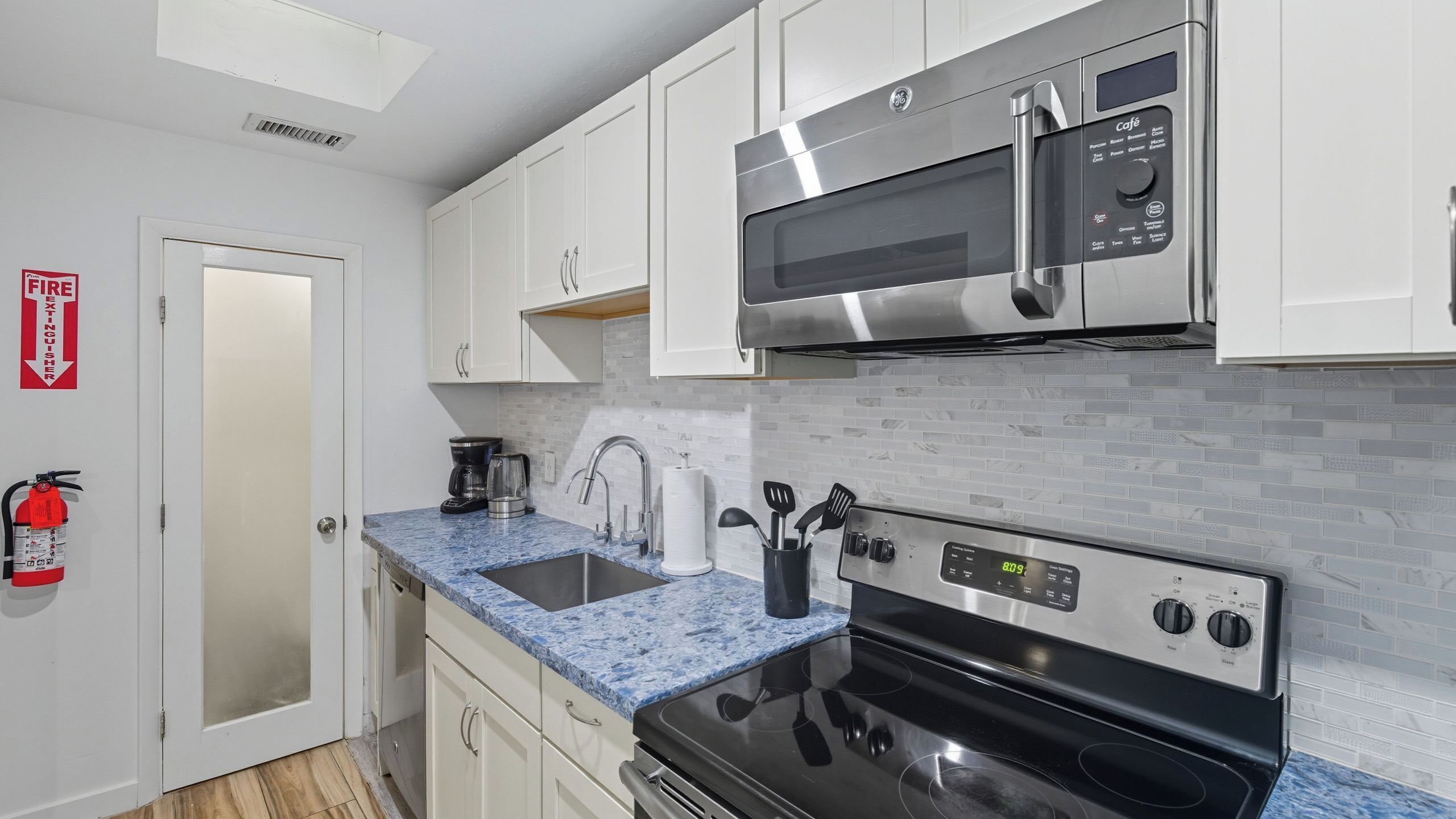 A modern kitchen with white cabinets, a stainless steel microwave, a black stove, and a blue marble countertop.