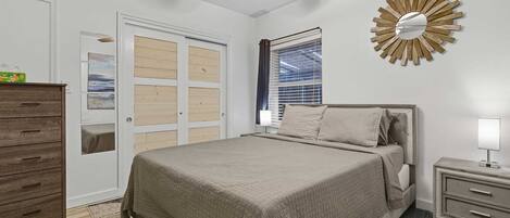 A bedroom with a bed, a nightstand, a dresser, a ceiling fan, and a window with blinds.