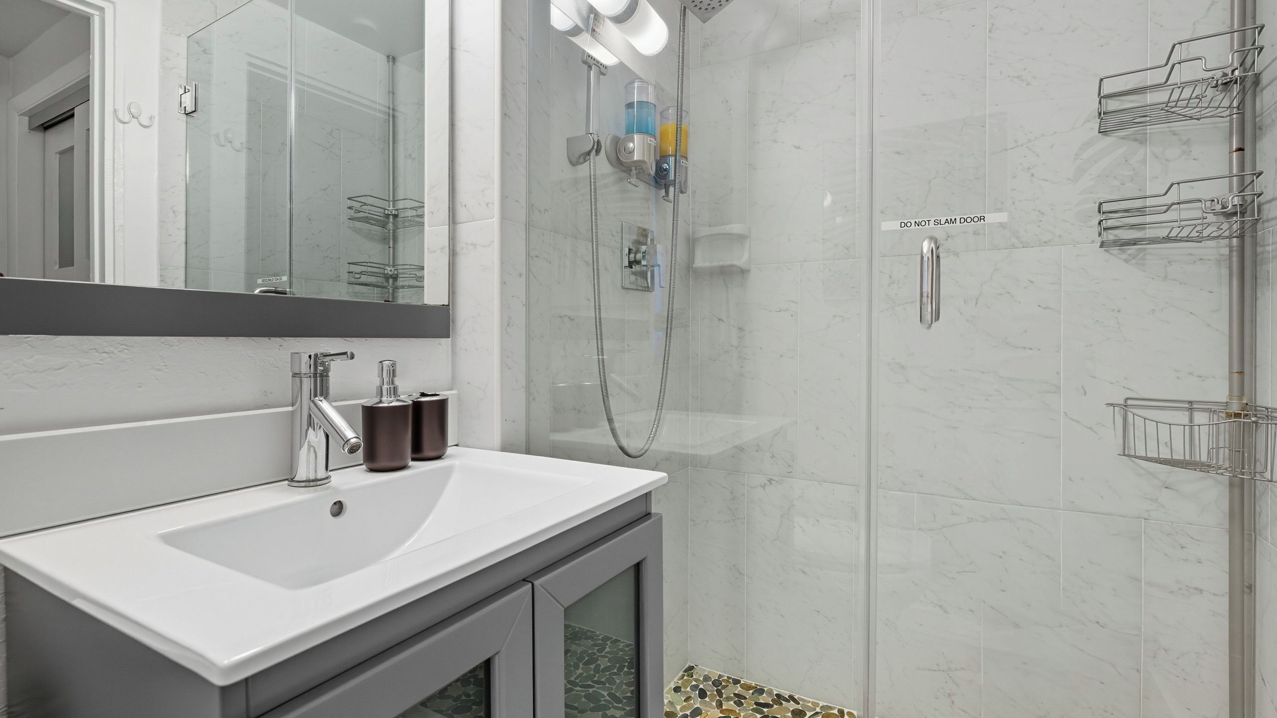 Ein modernes Badezimmer mit einem weißen Waschbecken, einer Duschkabine aus Glas und einer Wand mit Marmorplatten.