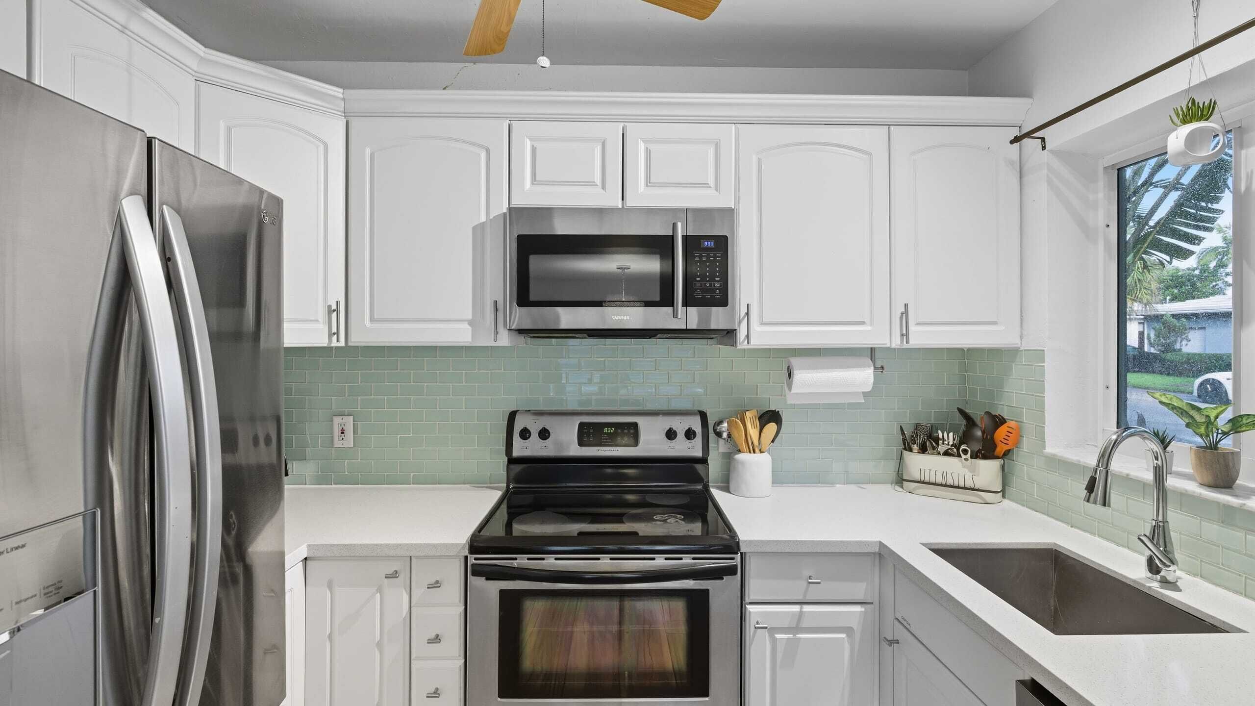 Una cocina moderna con armarios blancos, electrodomésticos de acero inoxidable y un salpicadero de azulejos verdes.