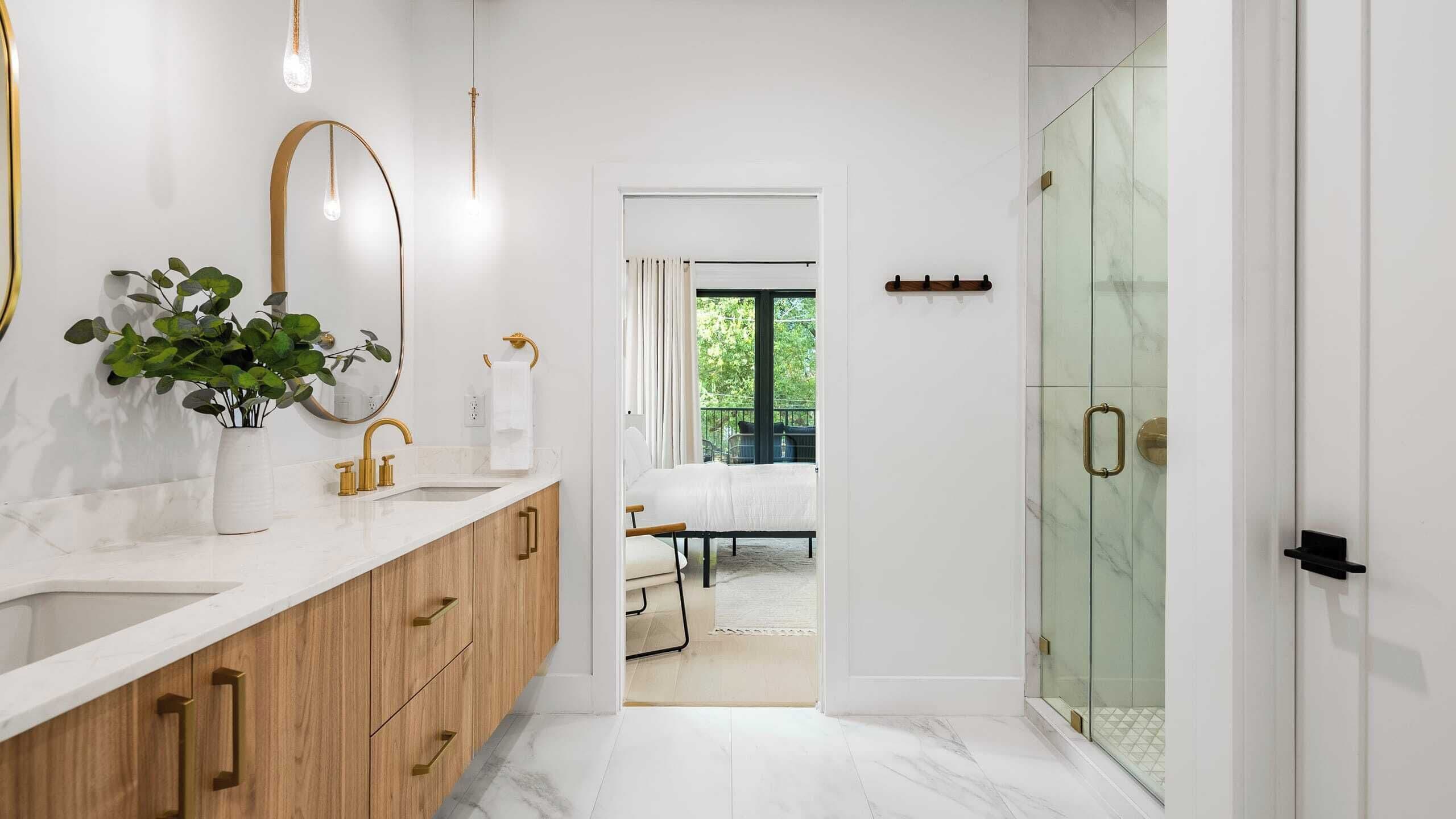 A modern bathroom with a double sink, a large mirror, and a potted plant.