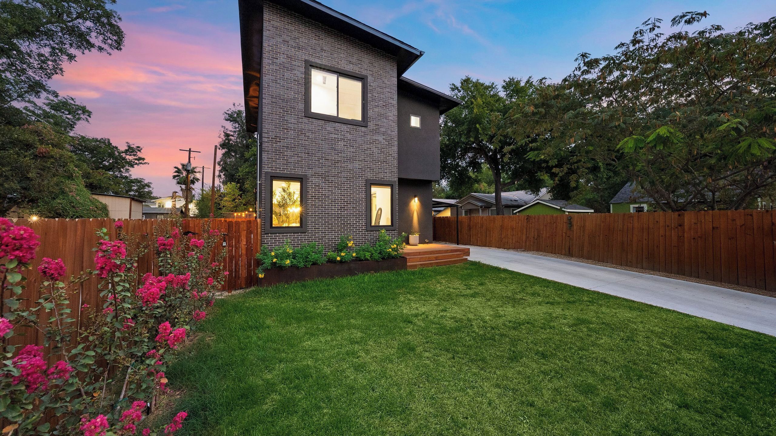 A modern two-story house with a well-maintained lawn and a wooden fence.