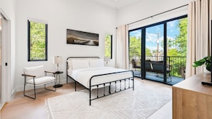 Une chambre à coucher comprenant un lit, une chaise, une table de chevet, une fenêtre, un balcon et un tableau accroché au mur.