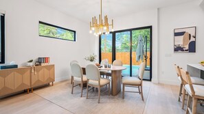 Un espace repas moderne avec une table ronde, des chaises, un buffet en bois et une vue sur le jardin à travers des portes vitrées.
