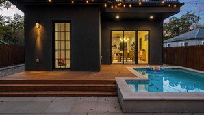 Ein modernes Haus mit Pool, Holzterrasse und einer Schiebetür zu einem Essbereich.
