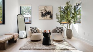 Ein modernes Wohnzimmer mit einem großen Spiegel, zwei Sessel, einem Couchtisch, einer Bank und einer Topfpflanze.