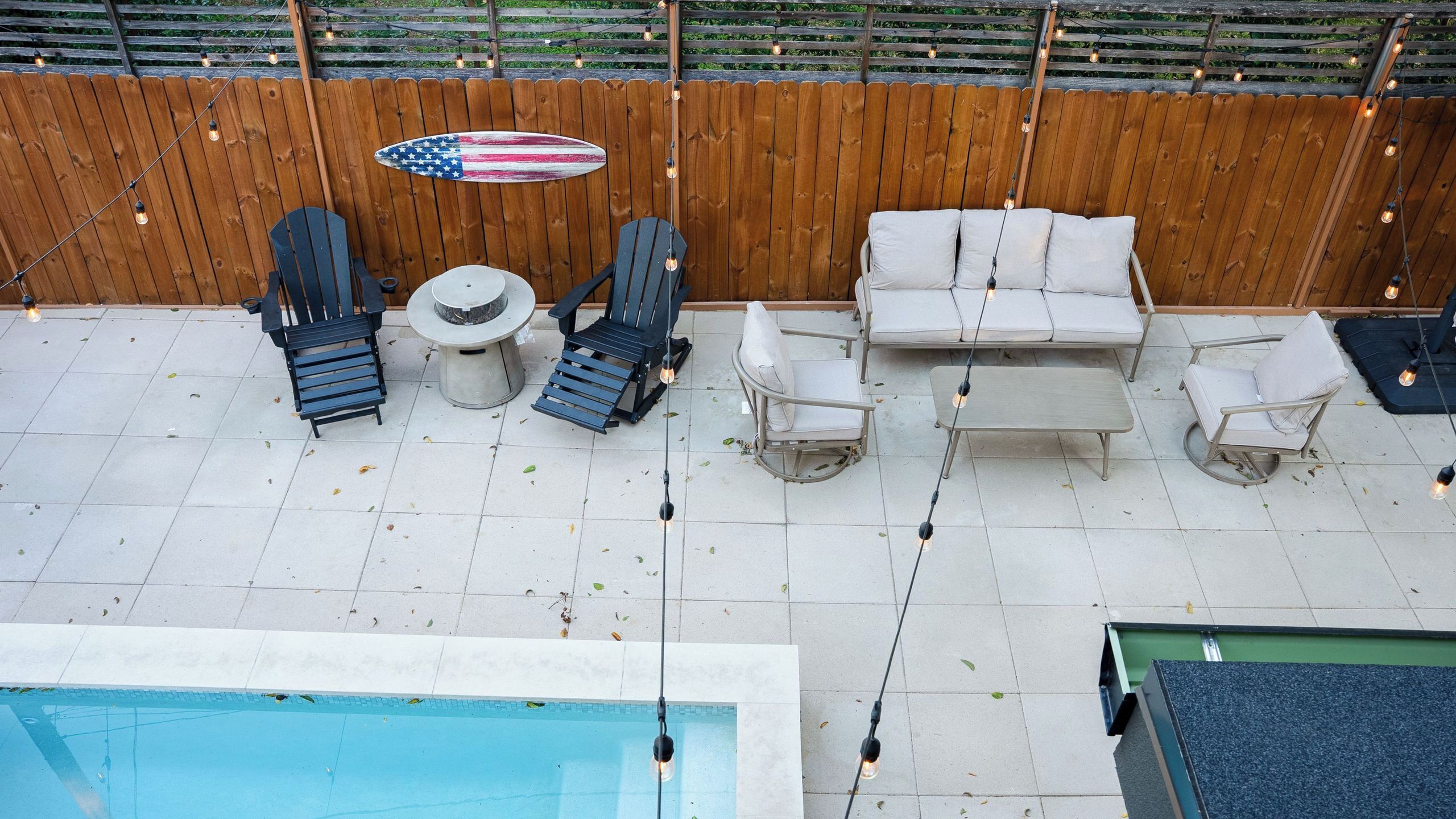 A poolside area with a wooden fence, American flag decoration, and outdoor furniture including chairs and a table.