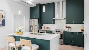 Une cuisine moderne avec des meubles de couleur vert foncé, des appareils en acier inoxydable, un îlot central doté de chaises et un éclairage suspendu.