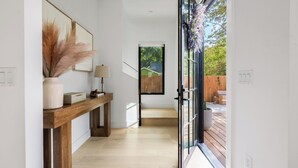 Ein modernes Interieur mit einem Holzkonsolentisch, einem gerahmten Kunstwerk, einer Lampe und Blick auf die Terrass.