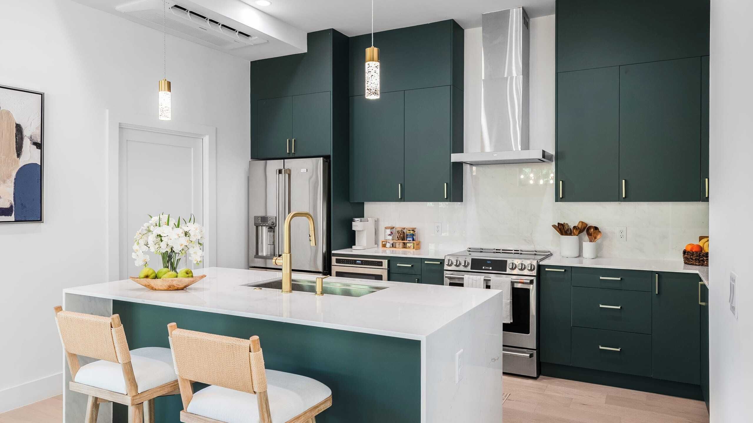 Een moderne keuken met donkergroene kastjes, roestvrijstalen apparatuur en een centraal kookeiland met zitplaatsen.