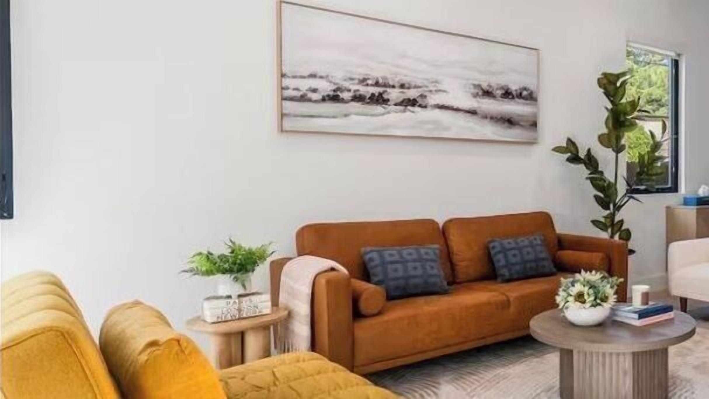 A living room with a brown sofa, a round coffee table, and a painting on the wall.