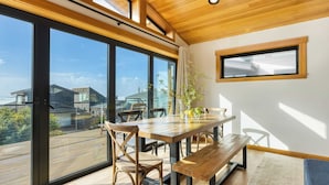 Un comedor con mesa y sillas de madera, ventanas amplias con vistas a edificios y una terraza.