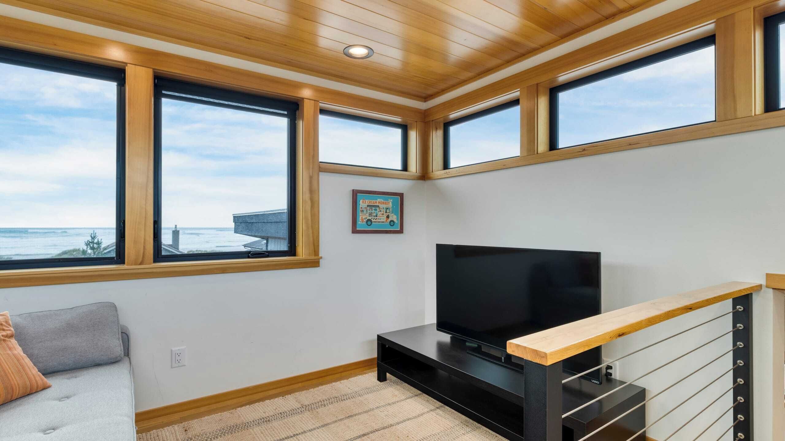 Una sala de estar moderna con ventanas amplias, un televisor de pantalla plana y techo de madera.