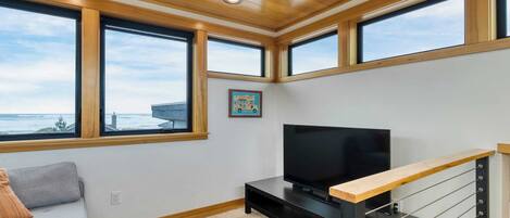 Una sala de estar moderna con ventanas amplias, un televisor de pantalla plana y techo de madera.