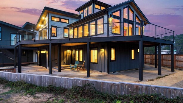 Una casa moderna de dos pisos con un porche cubierto, ventanas amplias y una terraza de madera.
