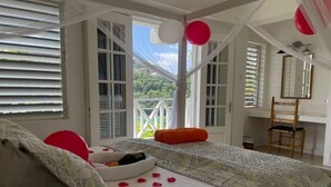 A bedroom with a bed, a window with blinds, a chair, and a view of greenery outside.