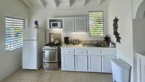 A compact kitchen with white cabinetry, a refrigerator, a stove, a microwave, and a sink.
