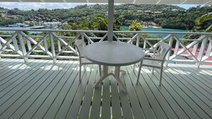 A covered outdoor area with a table and chairs, overlooking a scenic view of a harbor with boats and a hillside.