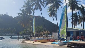 A beach with a row of boats, palm trees, and a building with a sign.
